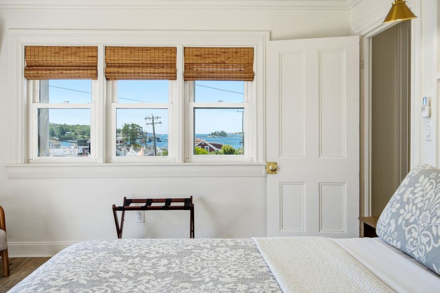 Bright guest room with a king bed and three windows overlooking Boothbay Harbor.